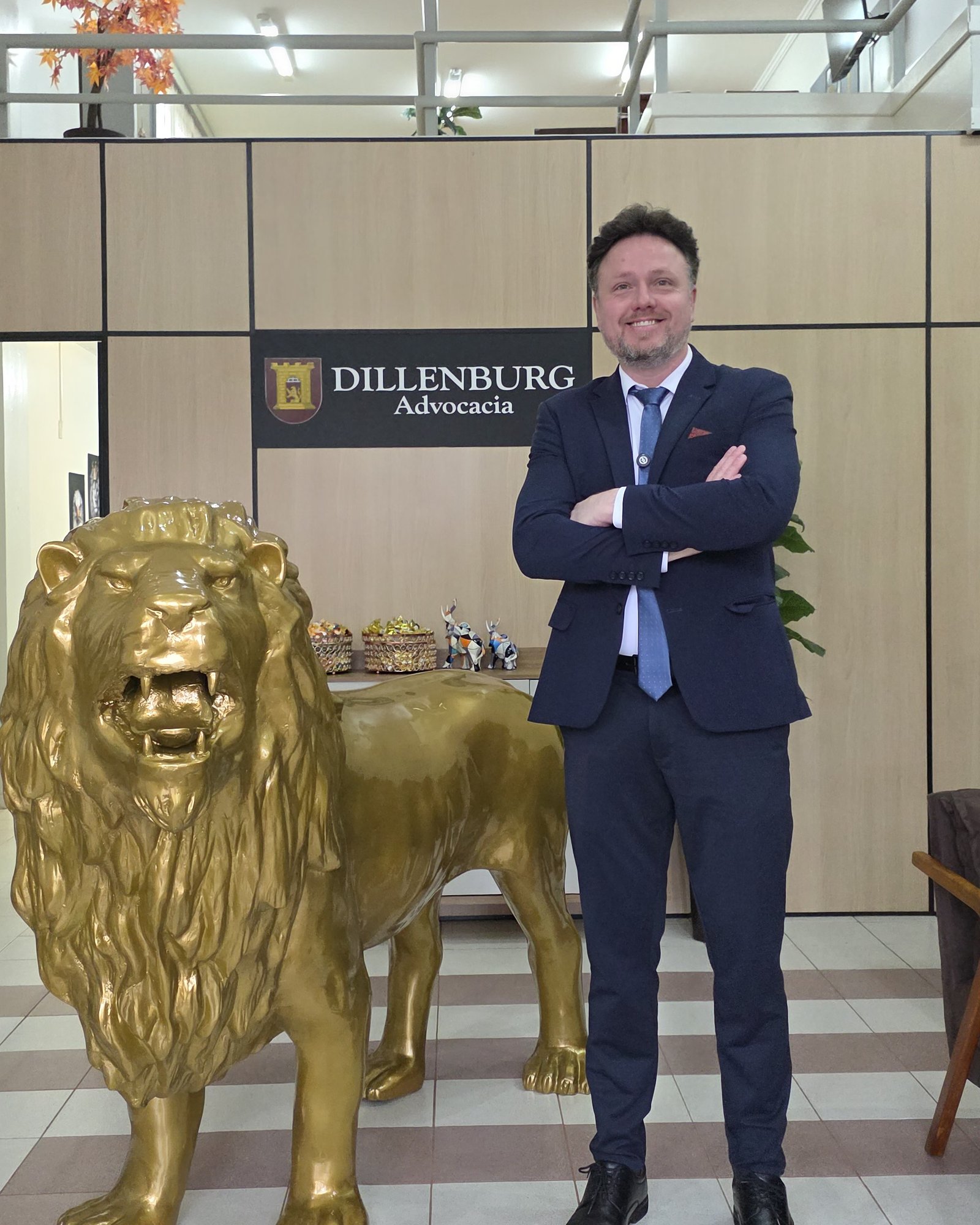 Dr. Cleber Dillenburg no escritório, ao lado da escultura de leão e da marca Dillenburg Advocacia